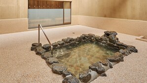 Una pequeña fuente de agua en el interior, rodeada de rocas, con un mueble de madera y puertas correderas al fondo.