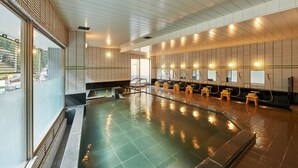 Una piscina interior moderna con pared de vidrio, listones de madera y varios taburetes a un lado.