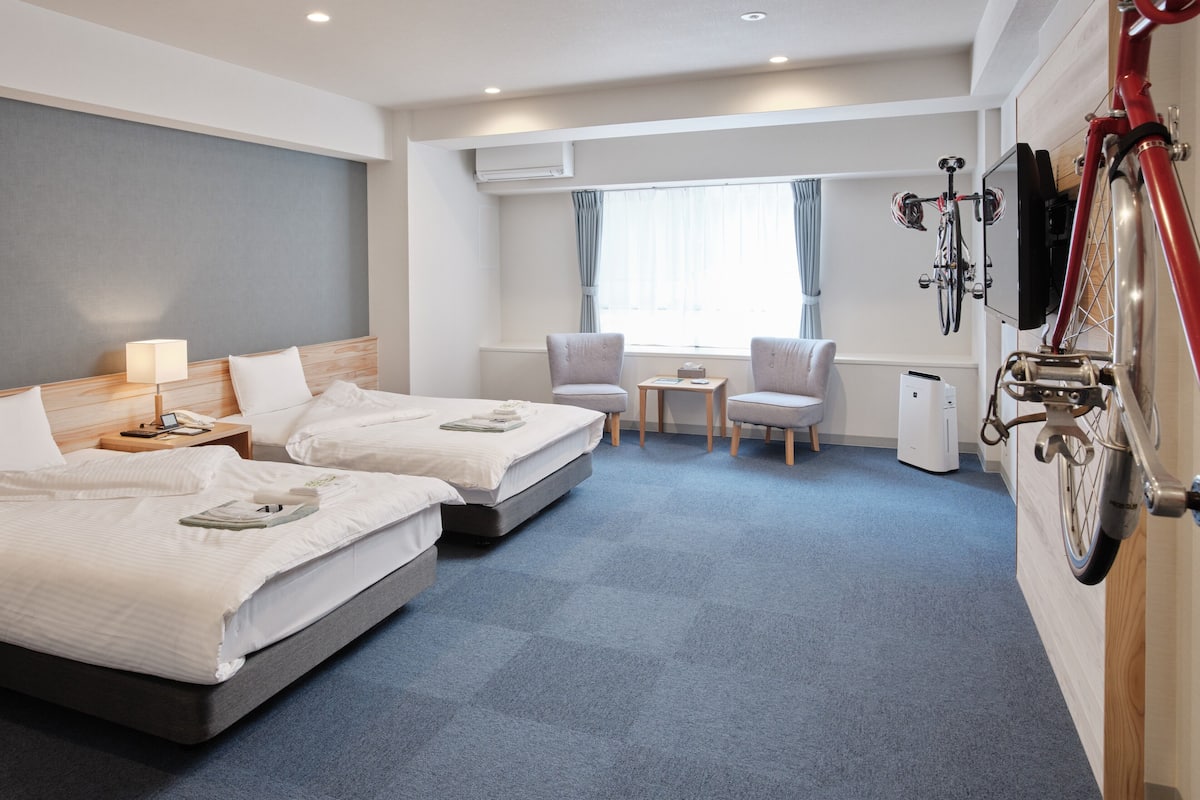 Habitación de hotel con dos camas, un escritorio, sillas y una bicicleta colgada en la pared.