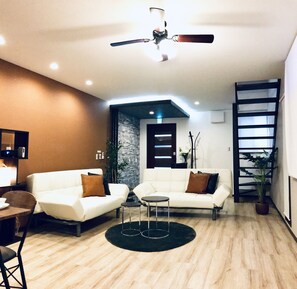 A modern living room with two white sofas, a small round table, and a ceiling fan. - TSUKI Tsuruhashi House (Osaka)