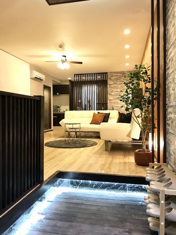 A modern living room with a white sofa, a small side table, a potted plant, and a wooden floor.