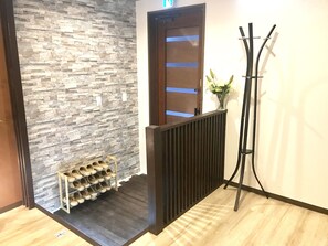 A hallway with a stone wall, a shoe rack, a coat rack, and a door with a blue stripe. - TSUKI Tsuruhashi House (Osaka)
