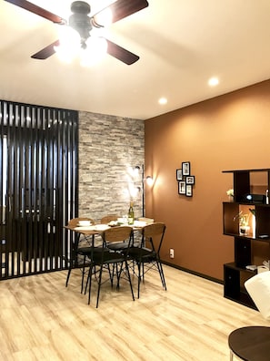 A dining area with a round table, chairs, a ceiling fan, and a stone wall.