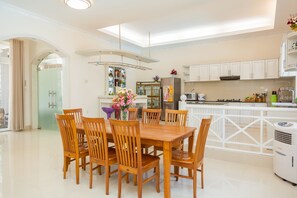 A modern kitchen with white cabinetry, a dining area with wooden chairs, and a central island with a refrigerator and a microwave. - Villa Kim Minh 14 (Ho Chi Minh City)