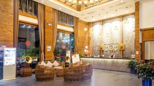 A hotel lobby with a wooden reception desk, wicker seating, and a large chandelier.