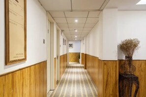 Een gang met houten lambrisering, een kamer met een patroon in de vloer en een bordje in de lijst aan de muur.