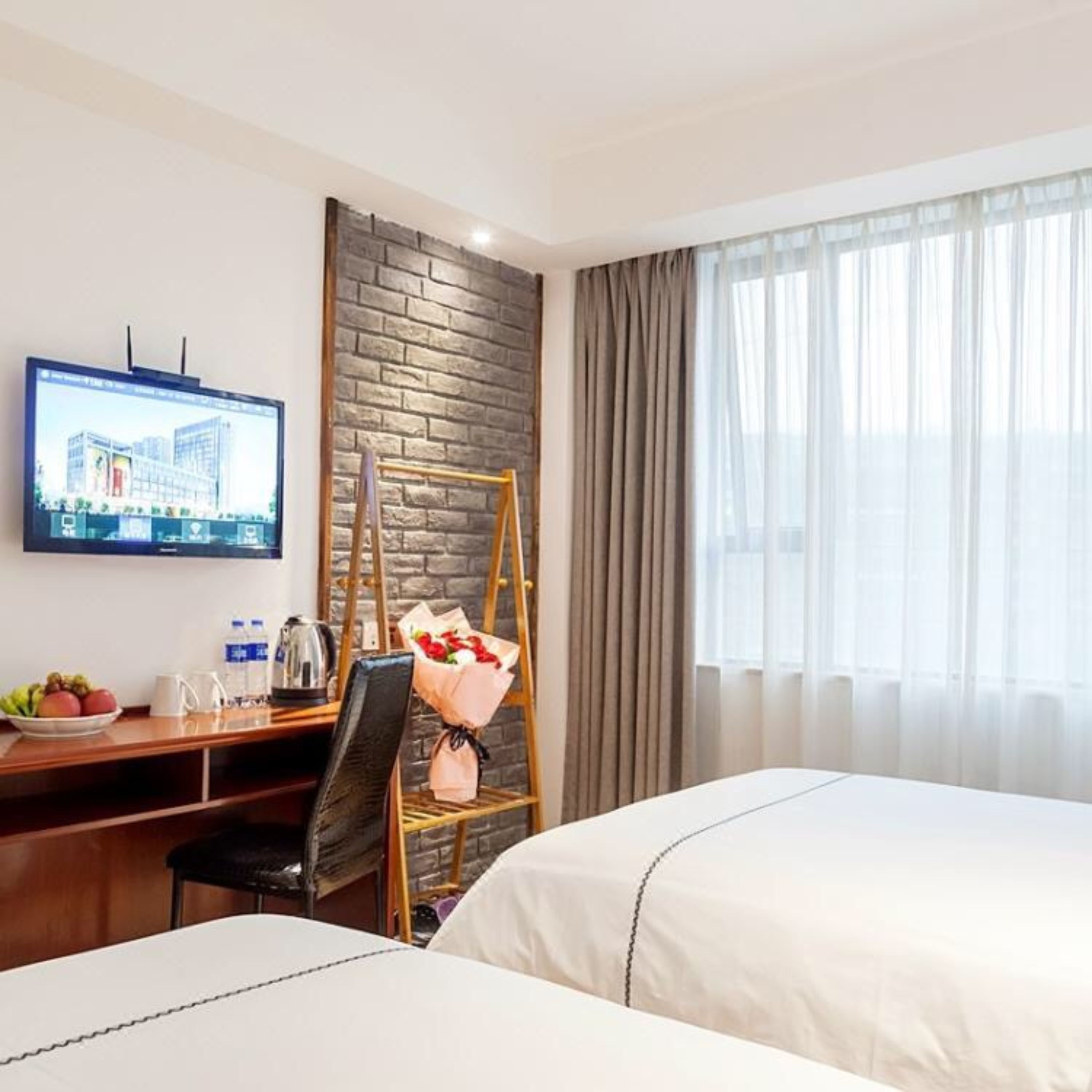A hotel room with two beds, a desk with a computer, a television, and a window with curtains.
