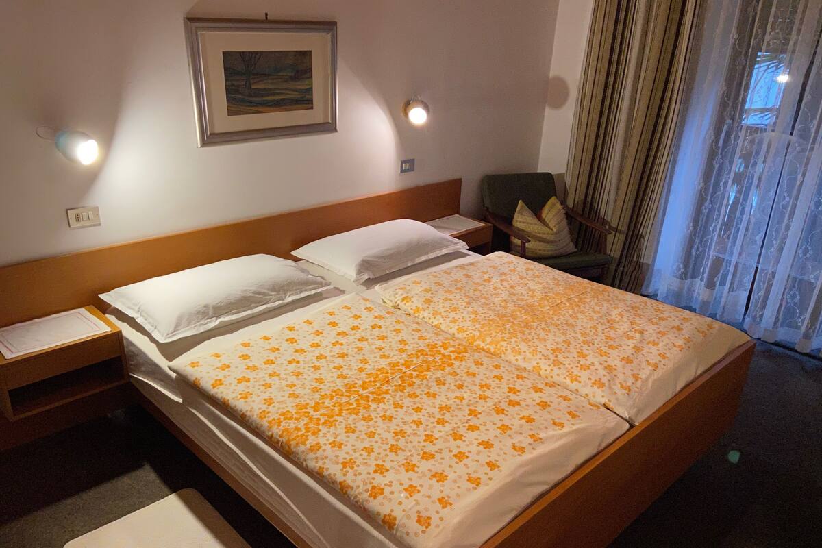 Ein Hotelzimmer mit einem großen Bett, zwei Nachttischen, einem Beistelltisch, einem Sessel, einem Fenster mit Vorhängen und einem gerahmten Bild an der Wand.
