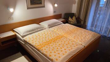 Una camera d'albergo con un letto grande, due comodini, una sedia, una finestra con tende e un quadro appeso al muro.