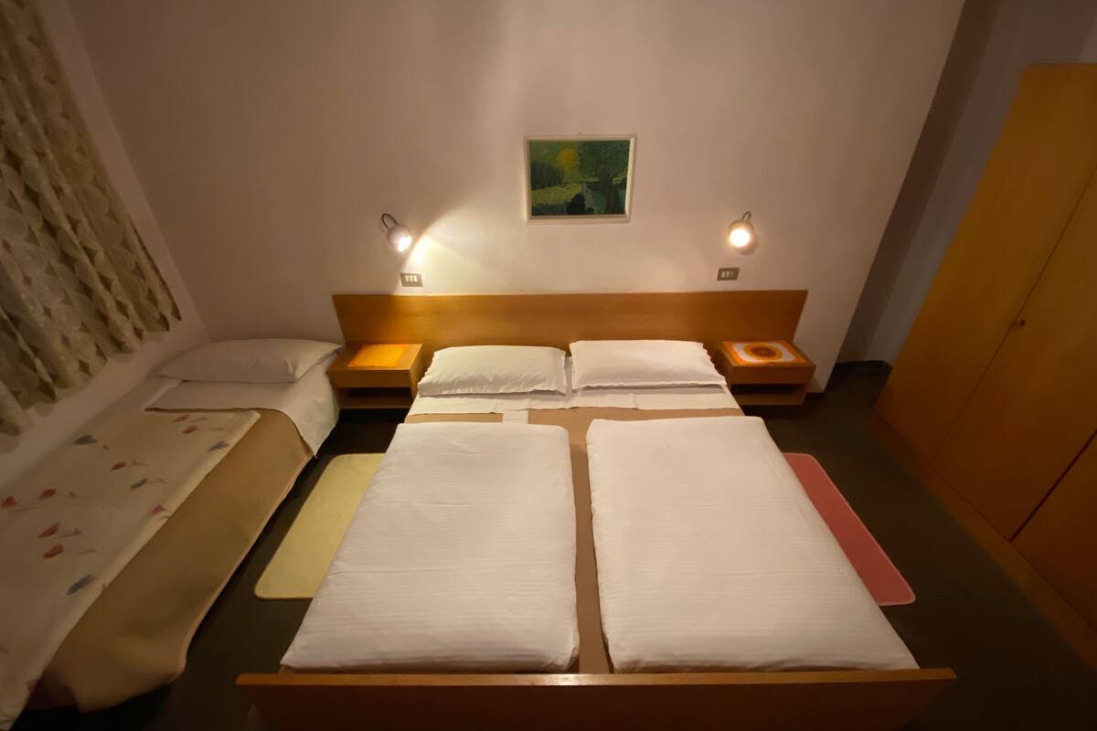 Ein Hotelzimmer mit einem großen Bett, zwei Nachttischen, einem kleinen Beistelltisch, einem Kleiderschrank und einem Bild an der Wand.