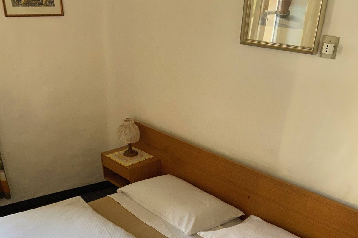 Ein Doppelbett mit weißer Bettwäsche, ein Holz-Kopfteil, ein Nachttisch mit Lampe und ein gerahmtes Bild an der Wand.