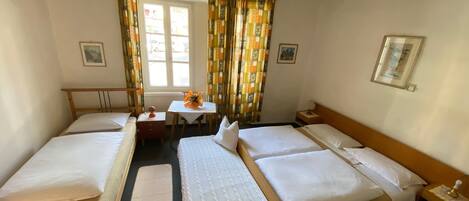 A hotel room with two single beds, a small table with a vase, and a window with curtains.