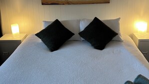 A bed with a white and blue striped bedspread, two black pillows, and a painting of a surfer on a beach.