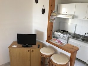 Une cuisine compacte équipée d’une cuisinière, d’un évier et d’un petit comptoir-bar en bois avec des tabourets.