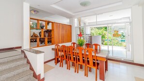 Un vaste espace dédié à la salle à manger, avec une table et des chaises en bois, un escalier et une vue sur la verdure grâce à de grandes portes vitrées.