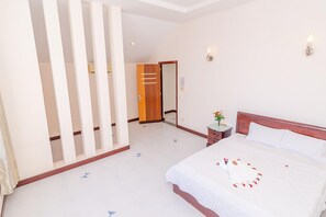 A hotel room with a large bed, a wooden wardrobe, a bedside table with a vase of flowers, and a mirror on the wall. - Villa Seaview 9 (Ho Chi Minh City)