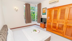 Une chambre à coucher avec un lit, une télévision, une armoire et une fenêtre avec des rideaux.
