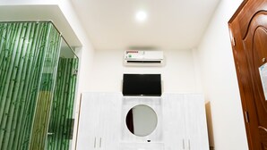 A bathroom with a bamboo shower curtain, a white vanity with a circular mirror, and a wall-mounted air conditioner. - Hoang Van Homestay Nha Trang (Bac Nha Trang)