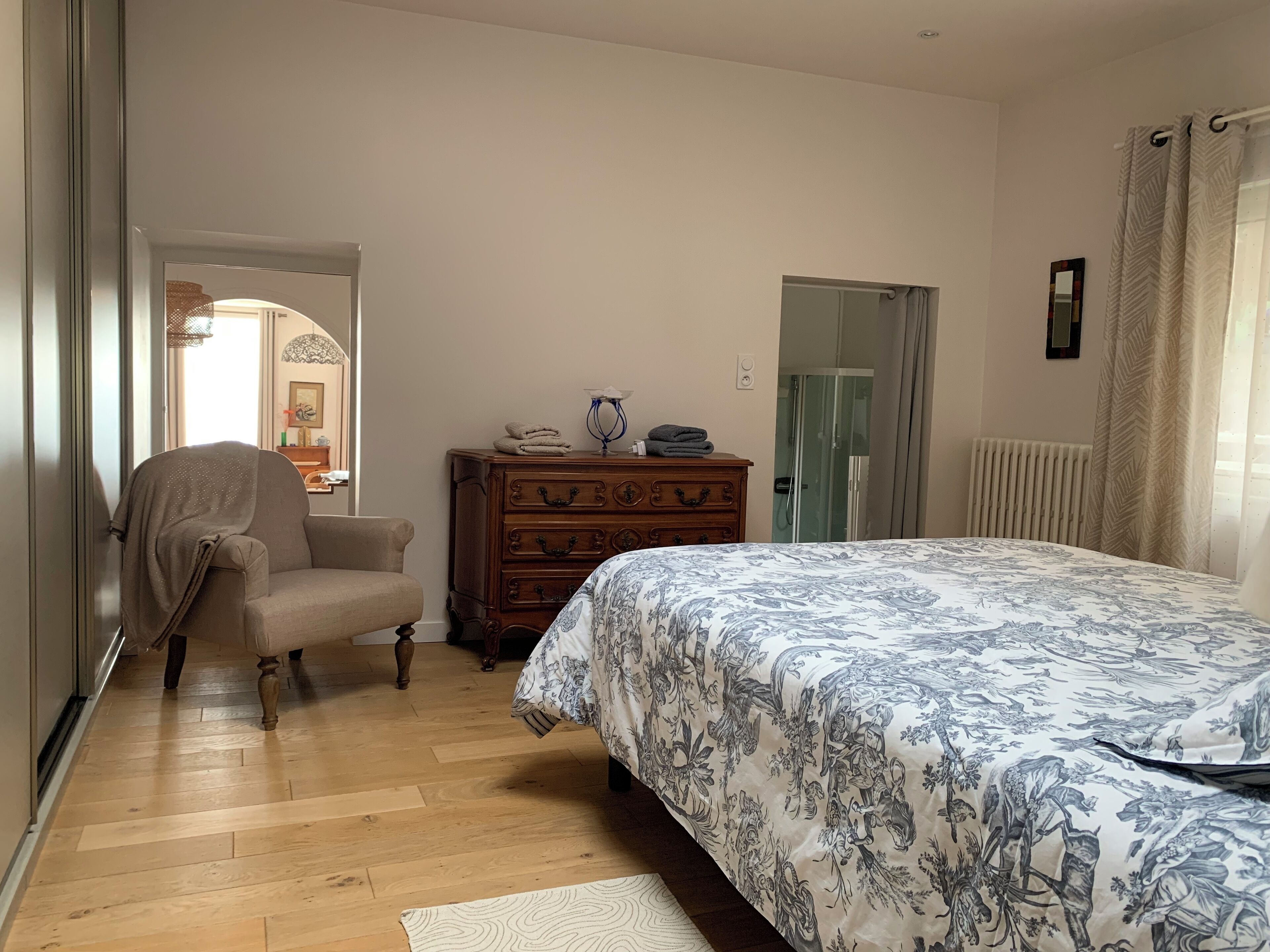 Quarto com cômoda de madeira, cama com colcha floral, uma cadeira e um radiador.
