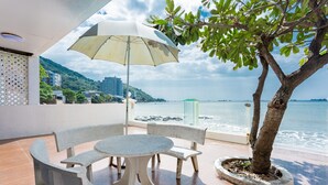 A balcony with a round table and chairs, a large umbrella, and a potted tree. - Villa Seaview 11 (Ho Chi Minh City)
