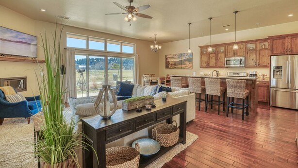 A spacious living area with a large window, a ceiling fan, and a kitchen with wooden cabinets and stainless steel appliances. - Steps to River, Yamaguchi Park, Air Conditioning and Downtown Fun! (Pagosa Springs)