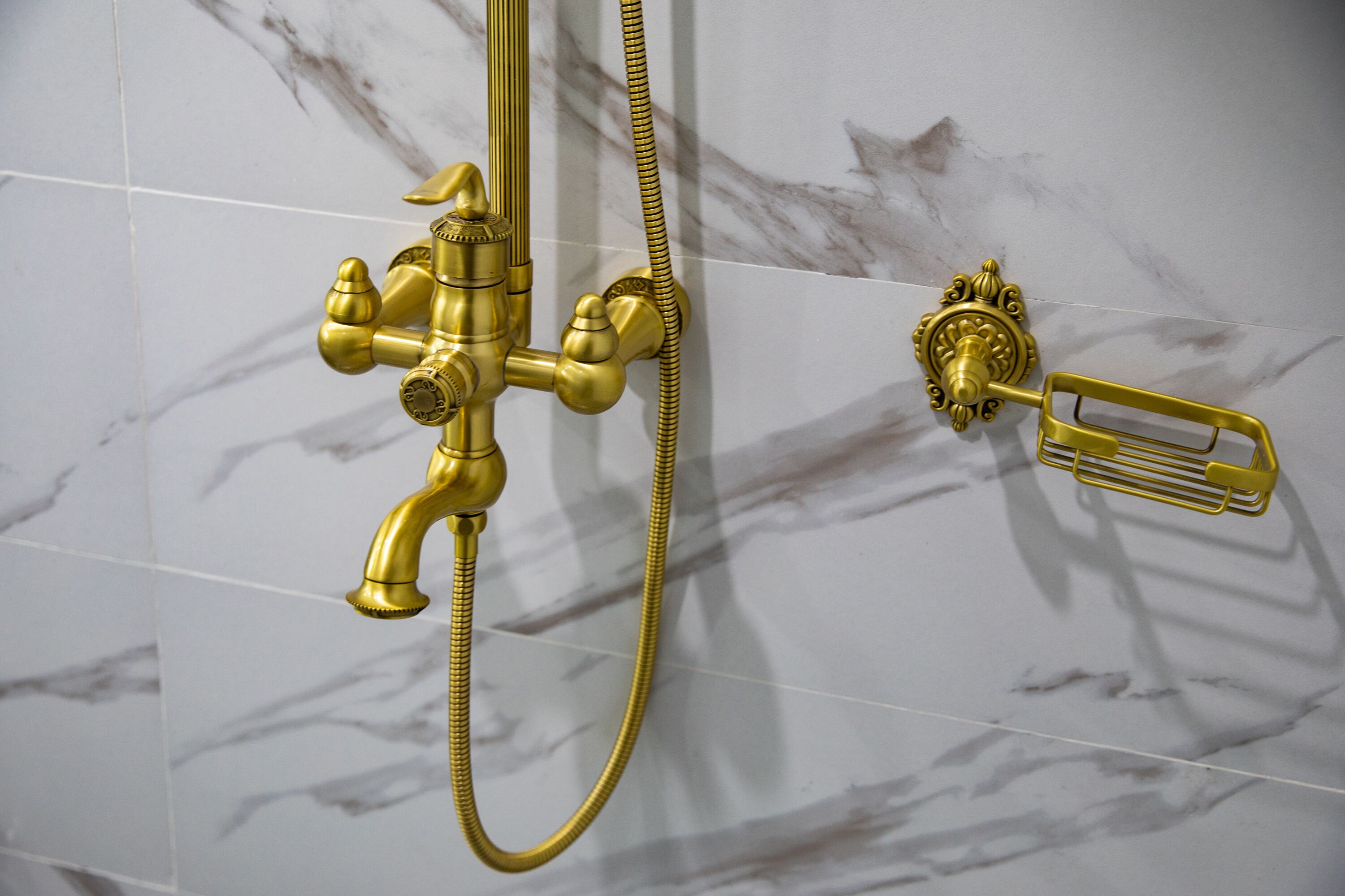 A gold showerhead and hose against a marble wall.