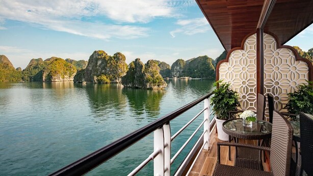 A balcony with a view of a calm river and rocky islands, furnished with wicker chairs and a glass table. - Aspira Cruises (Tuan Chau)