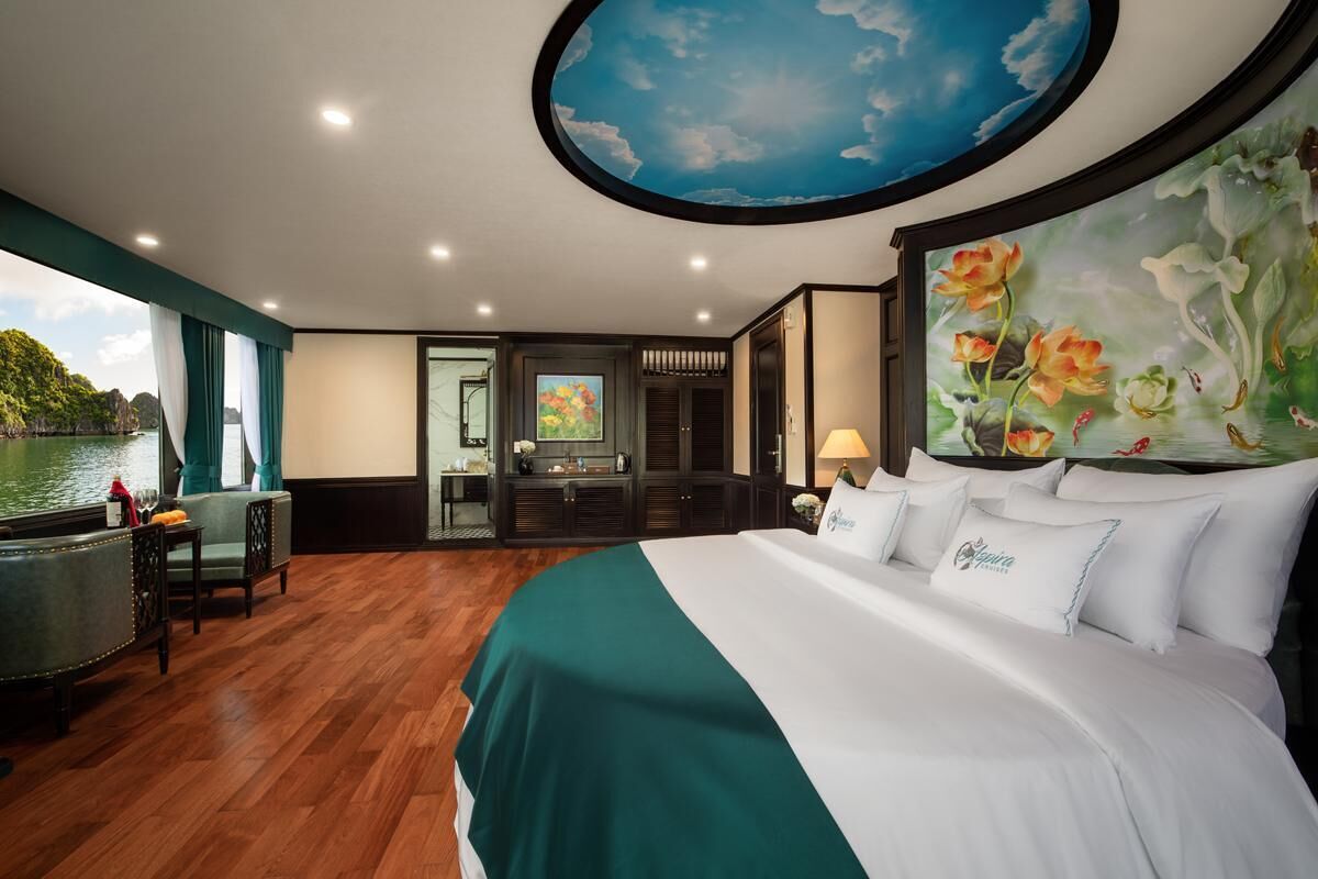 Quarto de hotel com uma cama grande, vista para a água, uma pintura de flores e um mural no teto.
