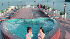 A hot tub surrounded by lounge chairs on a wooden deck with a view of the water and greenery. - Aspira Cruises (Tuan Chau)