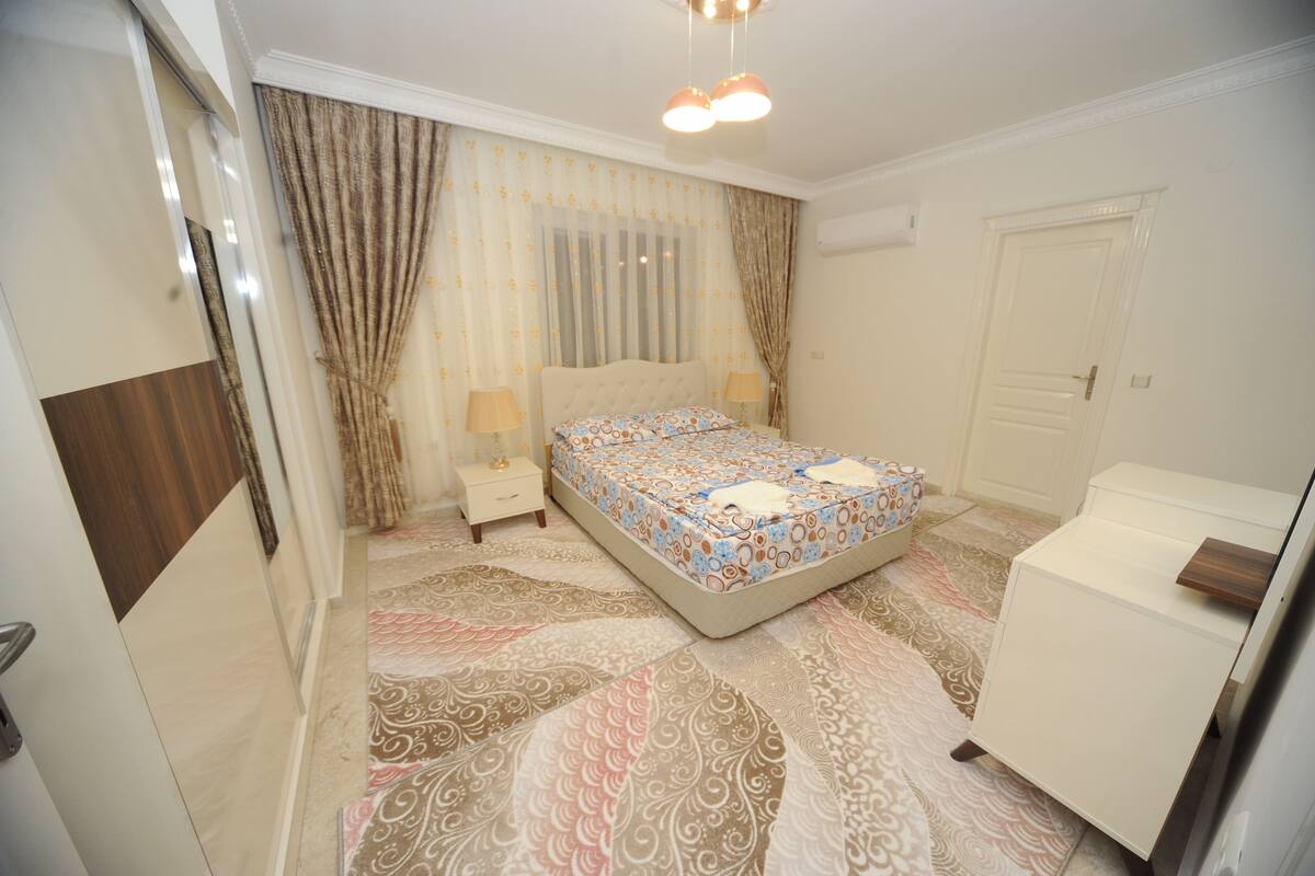 A bedroom with a bed, bedside tables, a wardrobe, and patterned carpet.