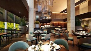 A modern dining area with multiple tables and chairs, large potted plants, and a bar area in the background. - Apartment Beach Nha Trang Sea View (Nha Trang)