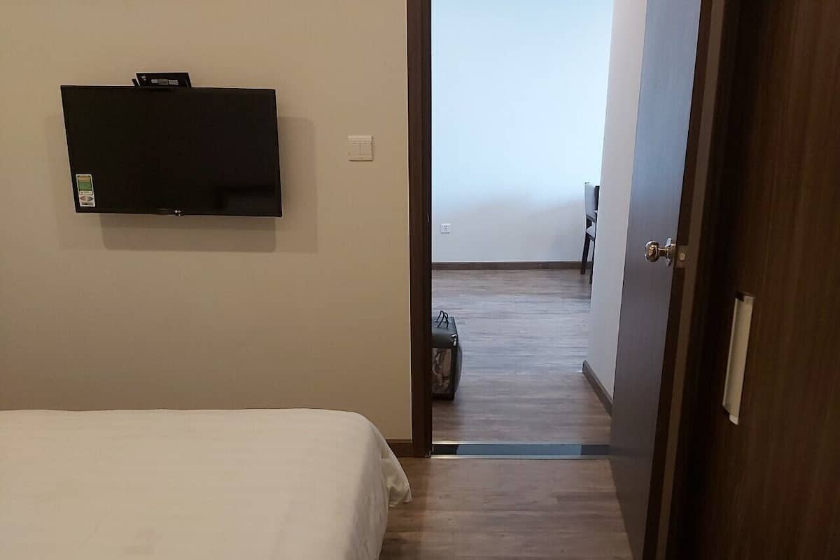 A hotel room with a bed, a flat-screen TV mounted on the wall, and a wooden floor.