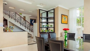 A dining area with a glass table and chairs, a staircase with a railing, and a bookshelf with plants. - Villa Seaview 1 (Ho Chi Minh City)