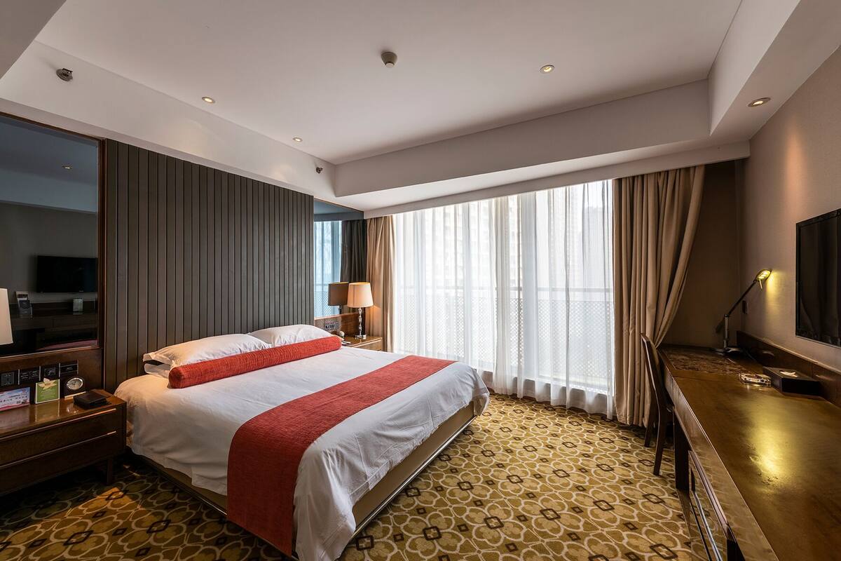 Een hotelkamer met een groot bed, een televisie, een bureau en een raam met gordijnen.