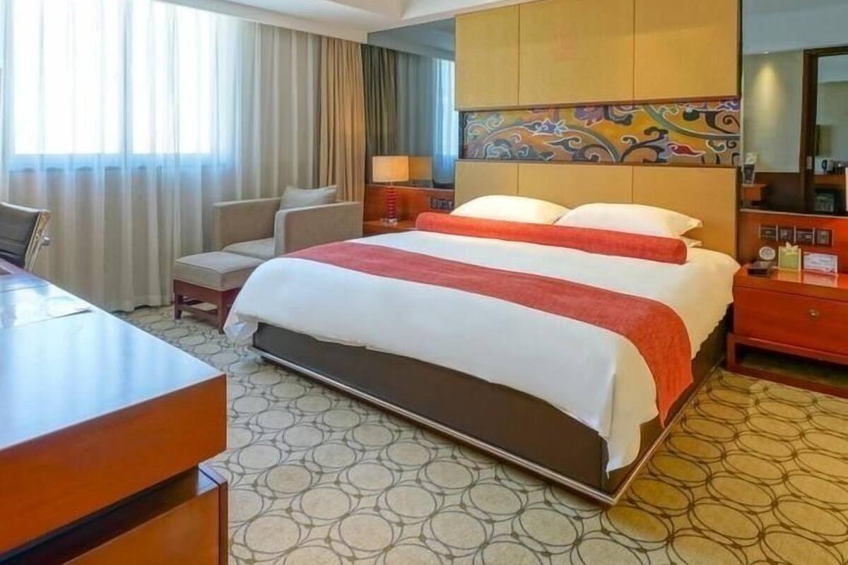Een hotelkamer met een groot bed, een bureau, een stoel en een groot raam met gordijnen.