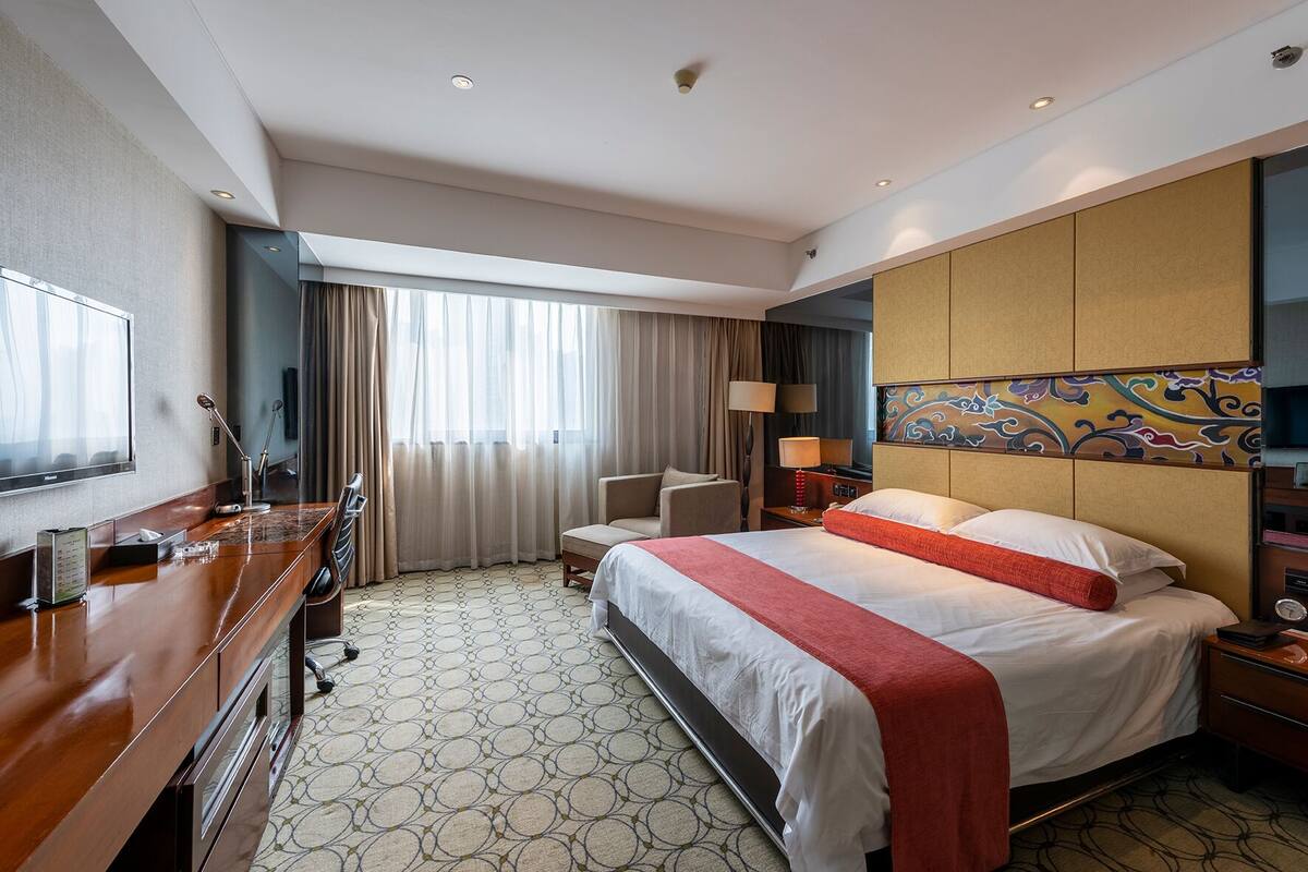 Een hotelkamer met een groot bed, een bureau met een computer, een stoel en een televisie.