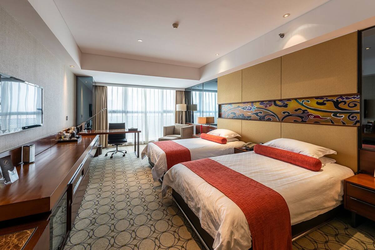 Een hotelkamer met twee bedden, een bureau, een televisie en een groot raam met gordijnen.