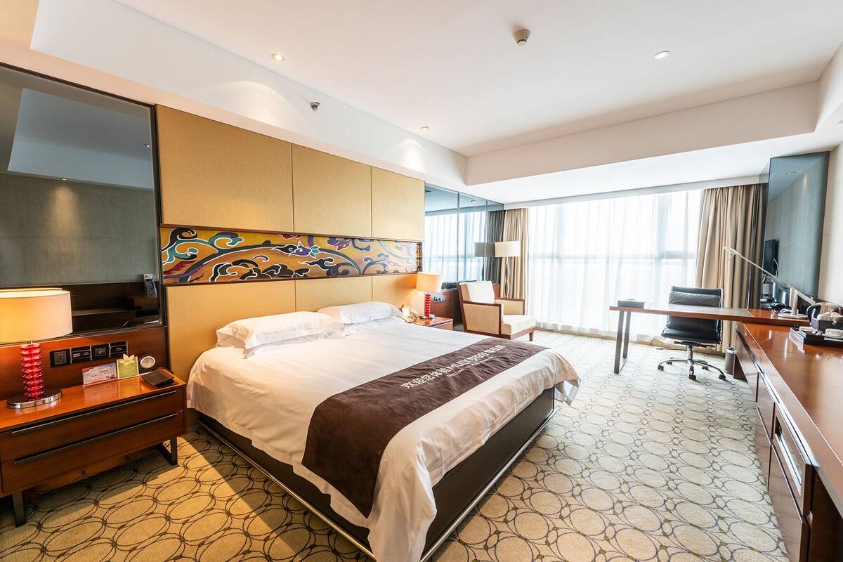 Een hotelkamer met een groot bed, een bureau, een stoel, een televisie en een decoratief hoofdeinde.