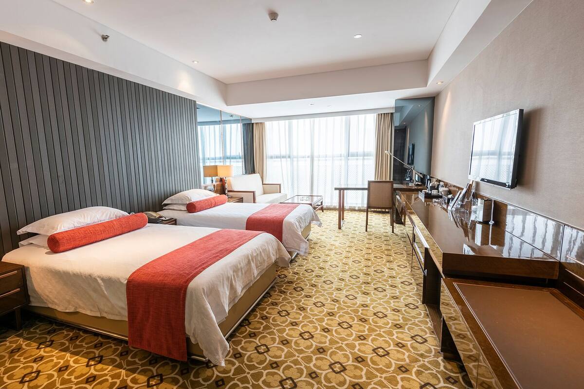 Een hotelkamer met twee bedden, een bureau, een stoel, een televisie en een groot raam.