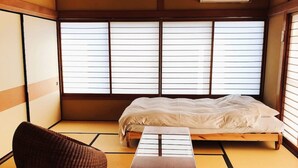 A traditional Japanese-style room with tatami flooring, a low wooden bed, a small table, and a cushioned chair.