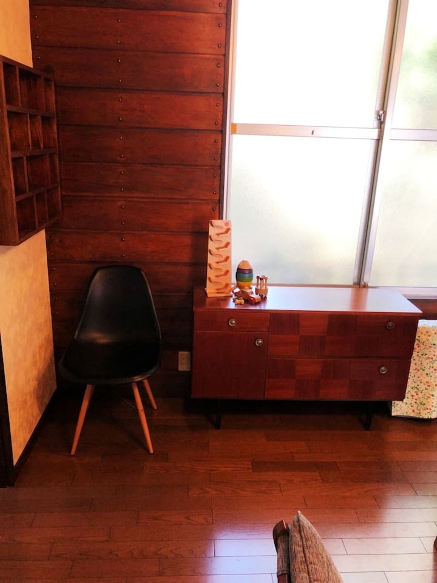 A room with wooden flooring, a black chair, a wooden dresser, and a window with a view.