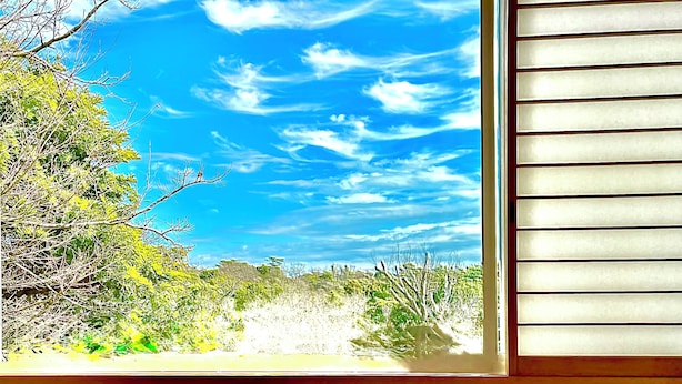 A room with a view of a natural landscape through a window, a wooden table, and a woven chair.