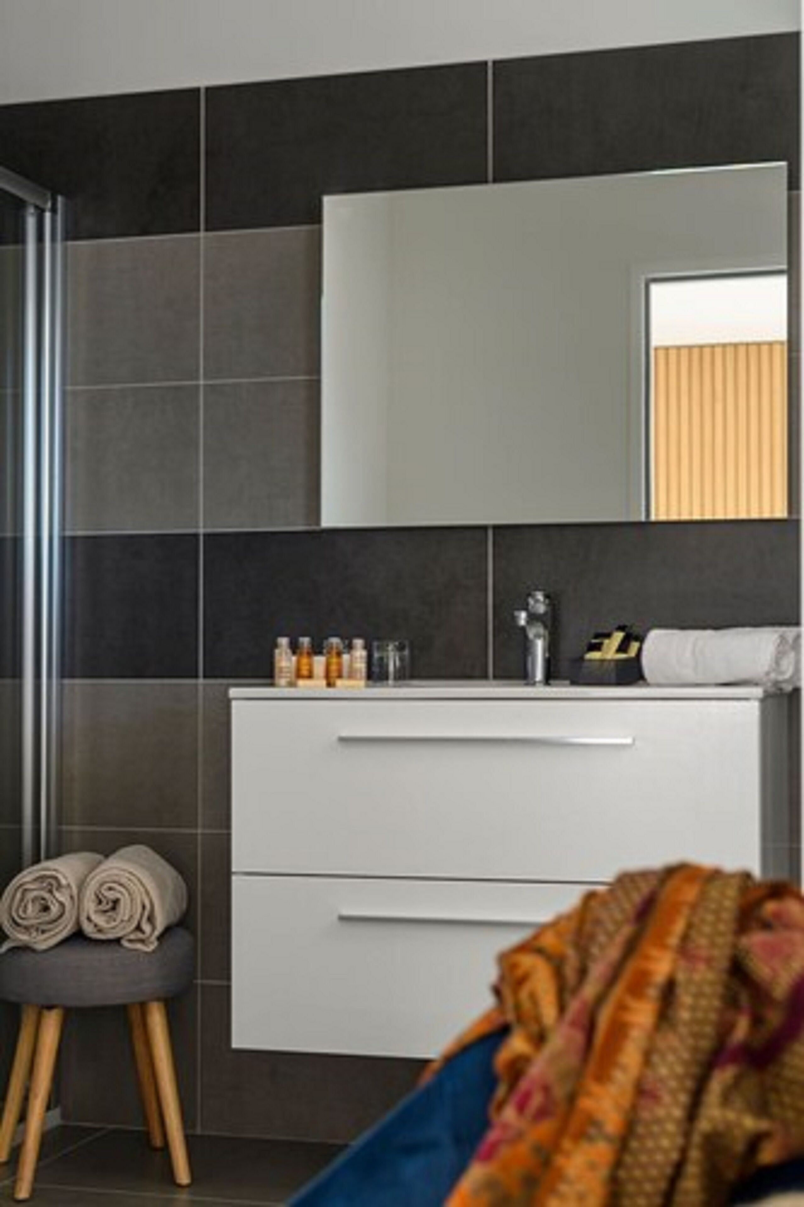 A modern bathroom with dark tiles, a white vanity, and a mirror.