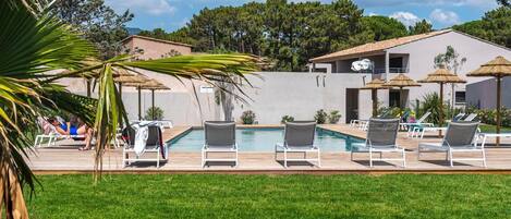 A pool area with lounge chairs and umbrellas, surrounded by greenery and buildings.