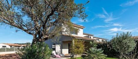 Une maison moderne avec un grand arbre dans le jardin, entourée d’un aménagement paysager bien entretenu.