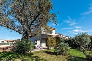 A modern house with a large tree in the front yard, surrounded by well-maintained landscaping.