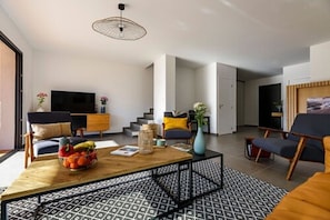 A modern living room with a sofa, coffee table, and TV. There are stairs leading to another room.