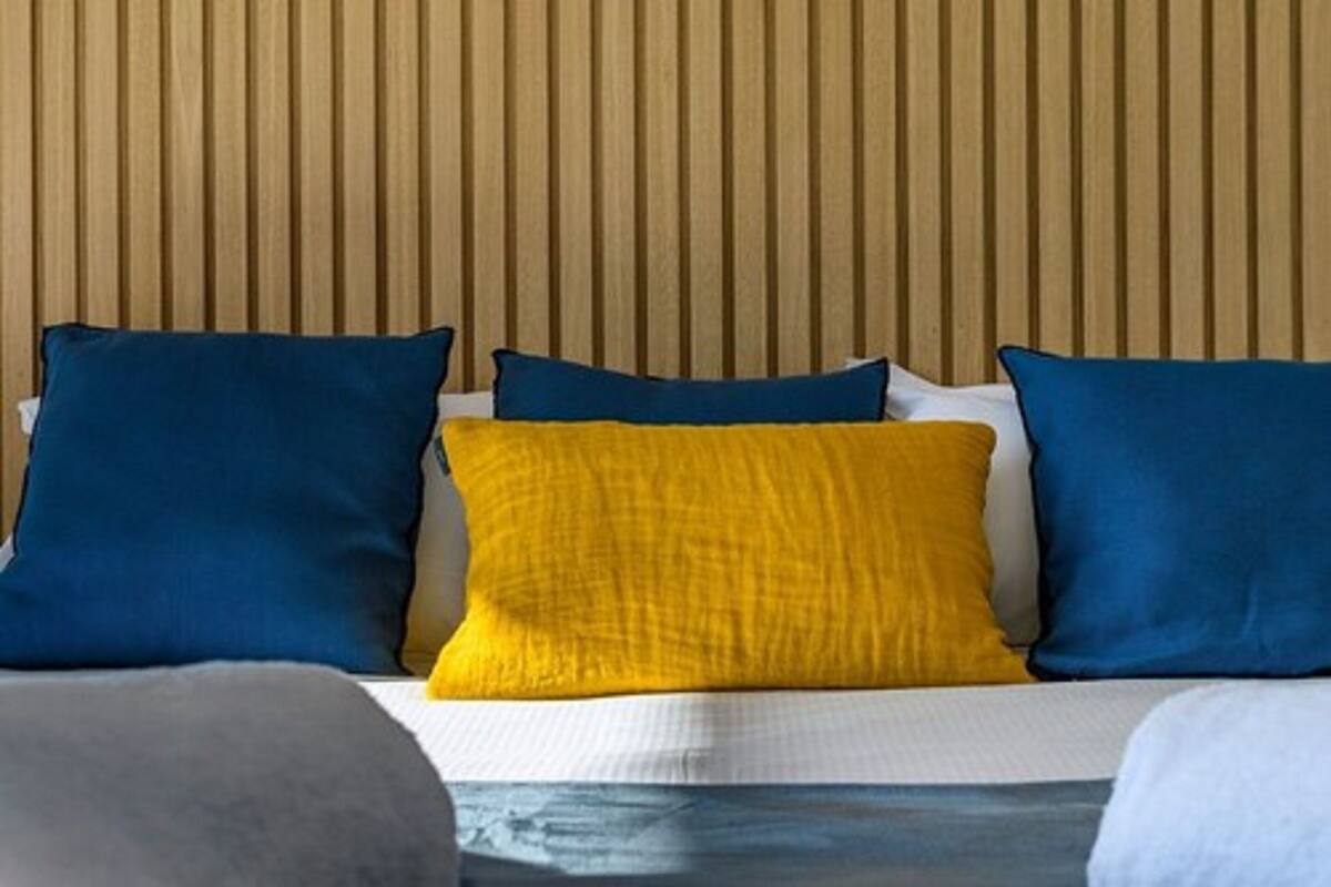 A bed with blue and yellow pillows, a wooden slat headboard, and a white bedspread.