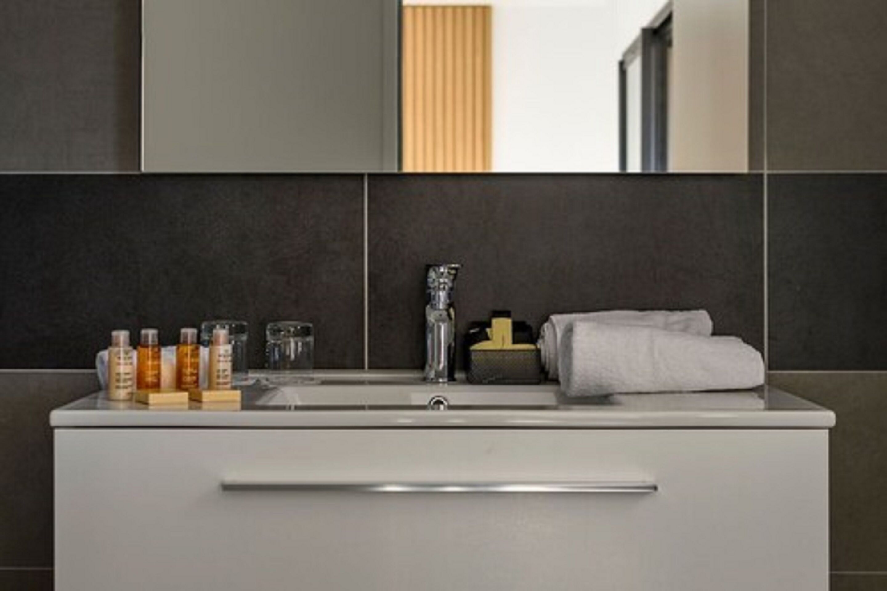 A modern bathroom with a white vanity, a mirror, and toiletries.