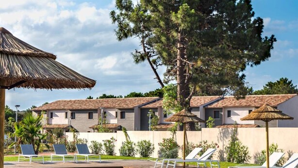 A swimming pool with lounge chairs and umbrellas, surrounded by buildings with a tiled roof. - Résidence Calarossa Bay Resort (Lecci)